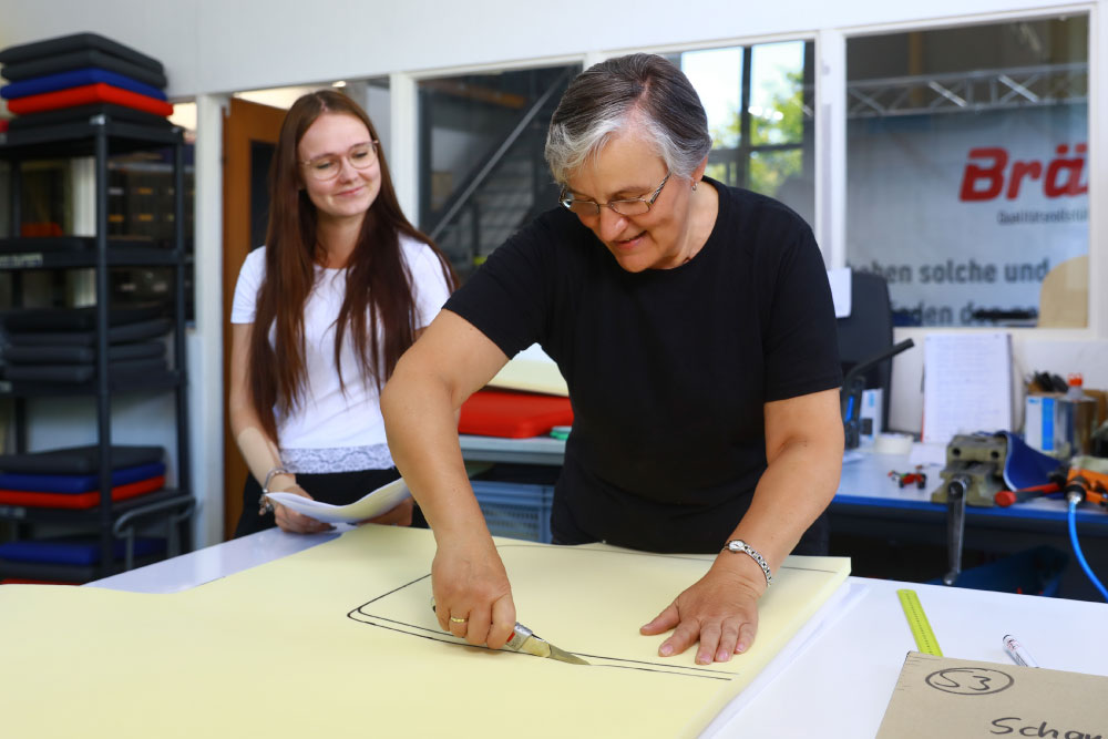 Praktikantin schaut einer Mitarbeiterin bei der Arbeit zu